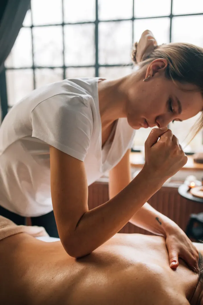 Therapist leaning in to apply forearm pressure along a guest's spine during a deep tissue session